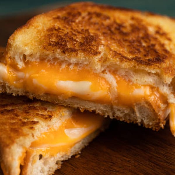 A grilled cheese sandwich, cut in half, revealing melted orange and white cheese oozing out.