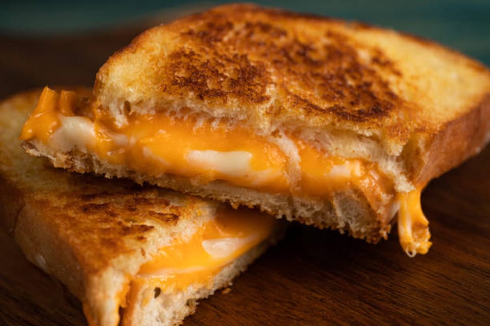 A grilled cheese sandwich, cut in half, revealing melted orange and white cheese oozing out.
