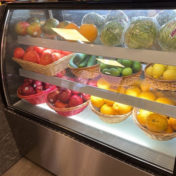 A refrigerated display case filled with fresh fruits and vegetables in woven baskets.