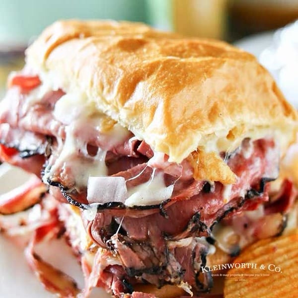 Close-up of a hot roast beef sandwich with melted cheese and onions, served with potato chips.